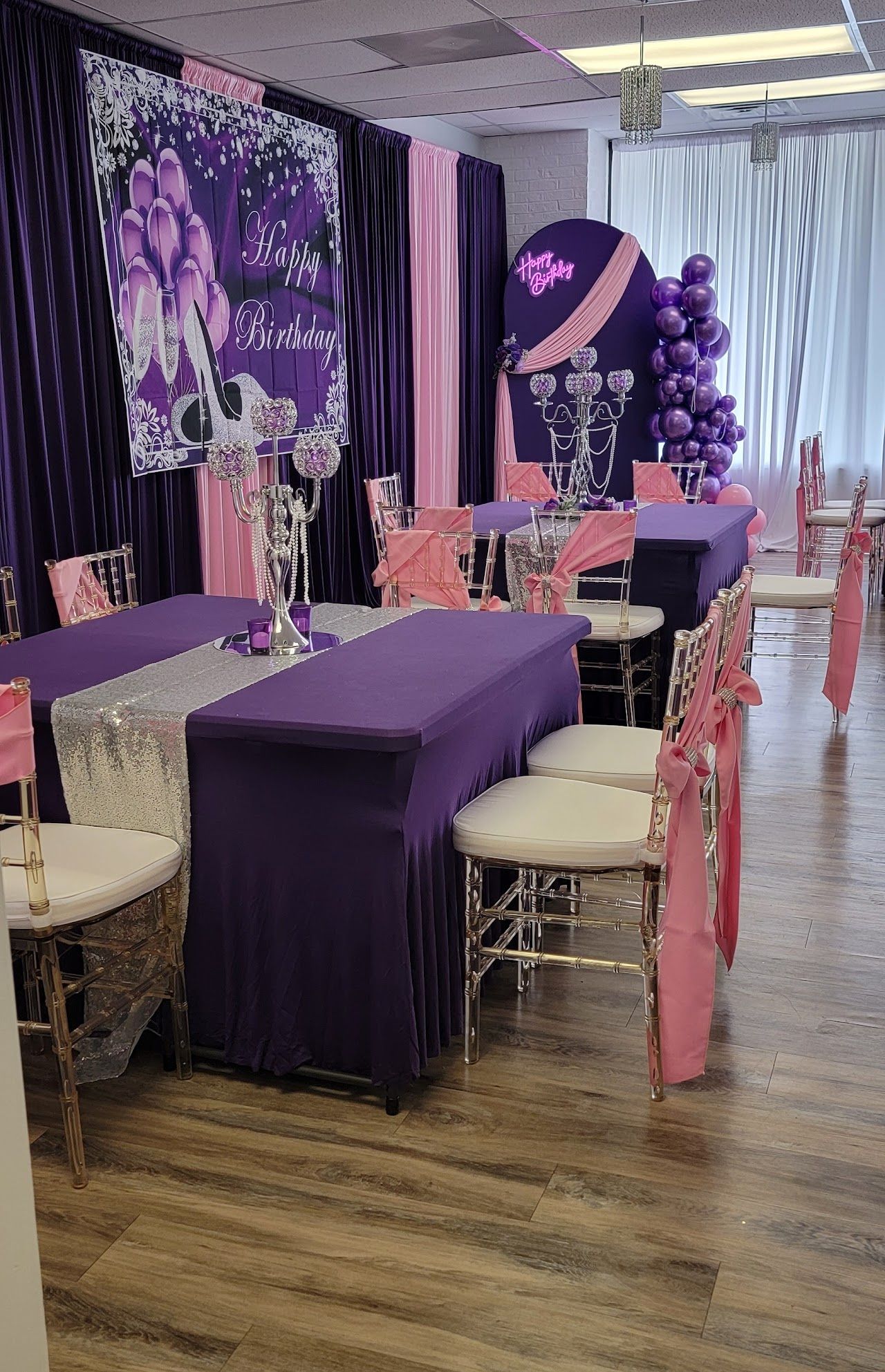 Purple and pink themed party decor with tables, chairs, and a backdrop.