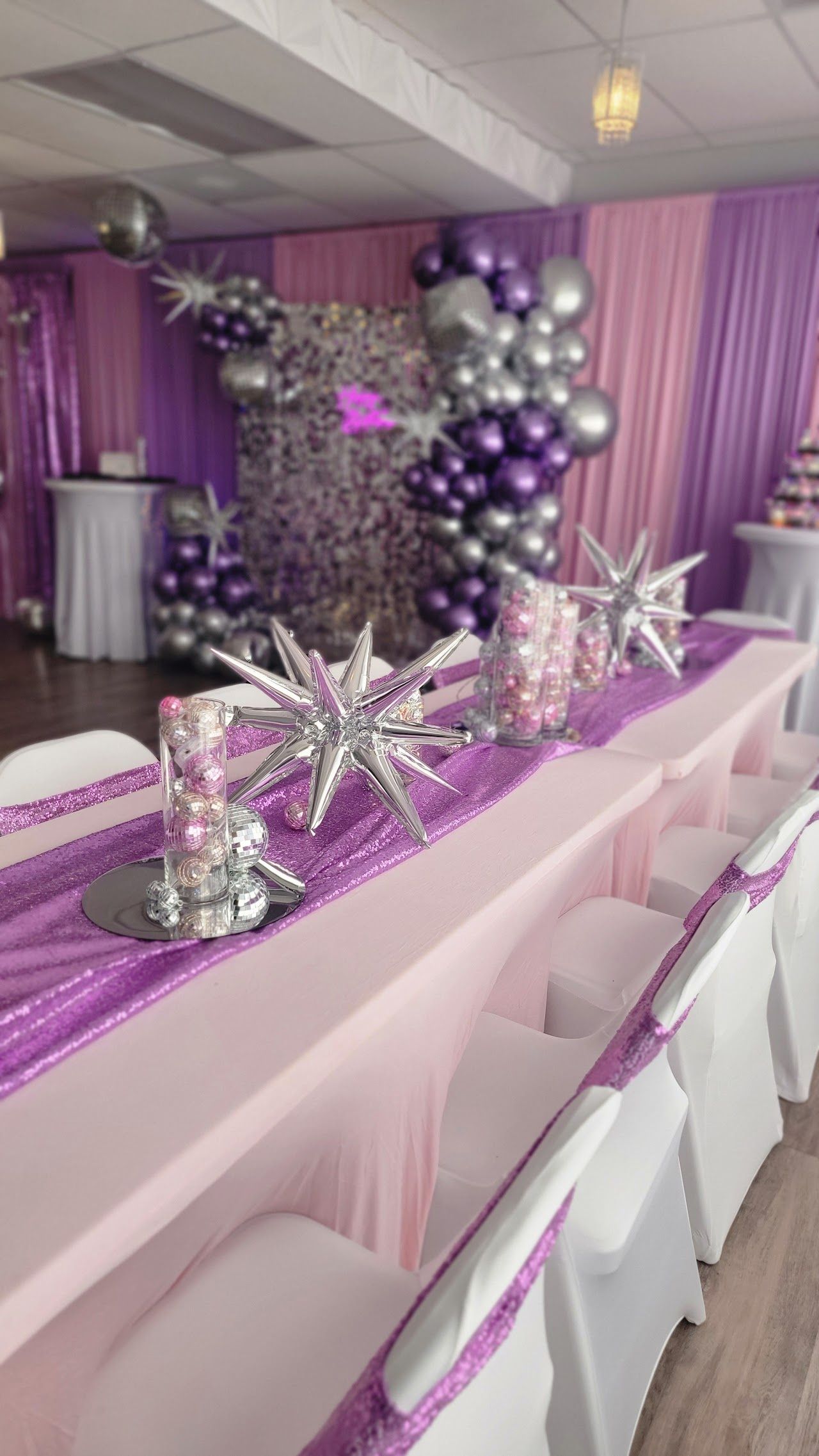 A long table decorated for a party, with purple and silver balloons and decorations.