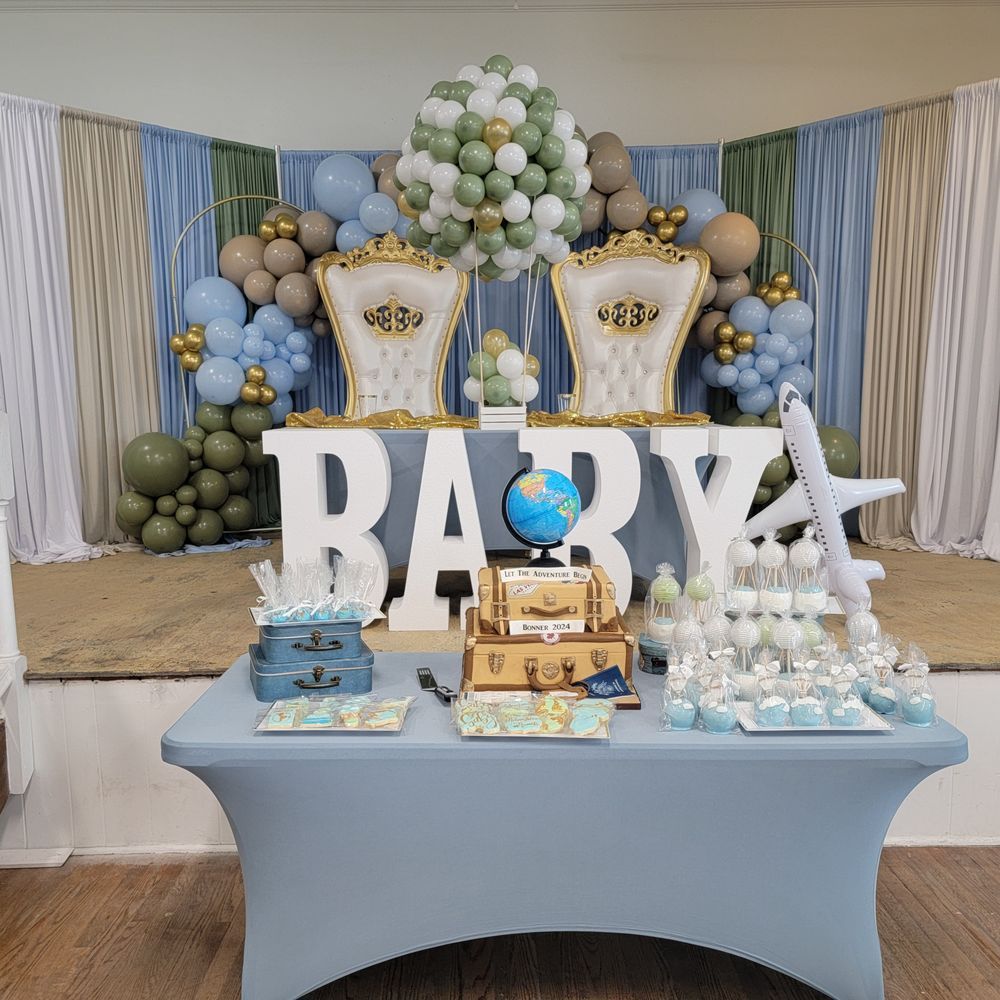 Baby shower with travel-themed decor: blue, green, gold balloons, airplane, suitcases, and globe on a blue table.