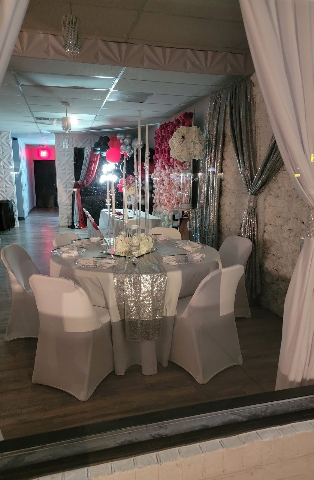 Formal event space: round table set for guests, adorned with flowers and silver accents, white chairs.