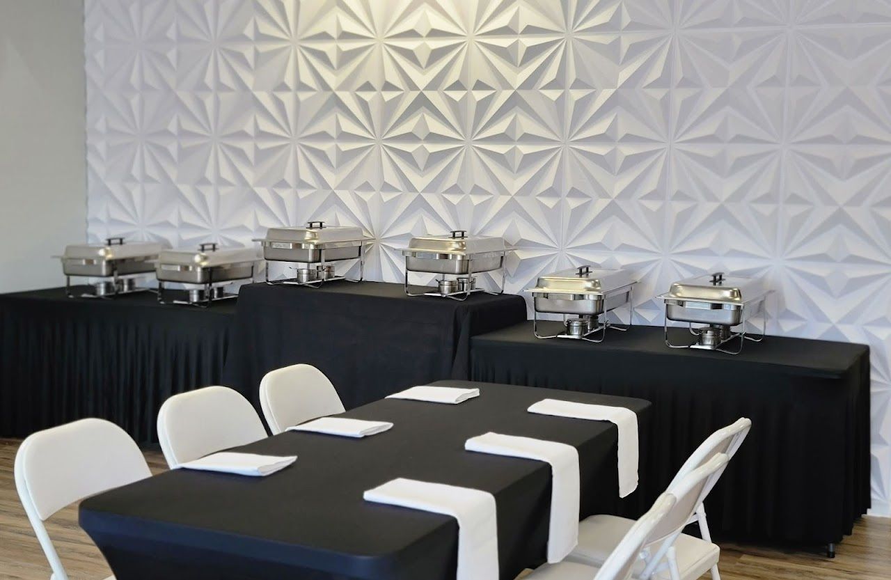 Buffet table with chafing dishes, table set for dining, against textured white wall.