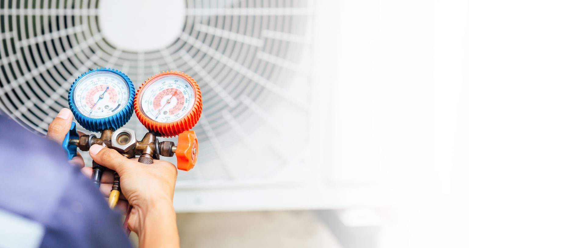 A person is holding two gauges in front of an air conditioner.