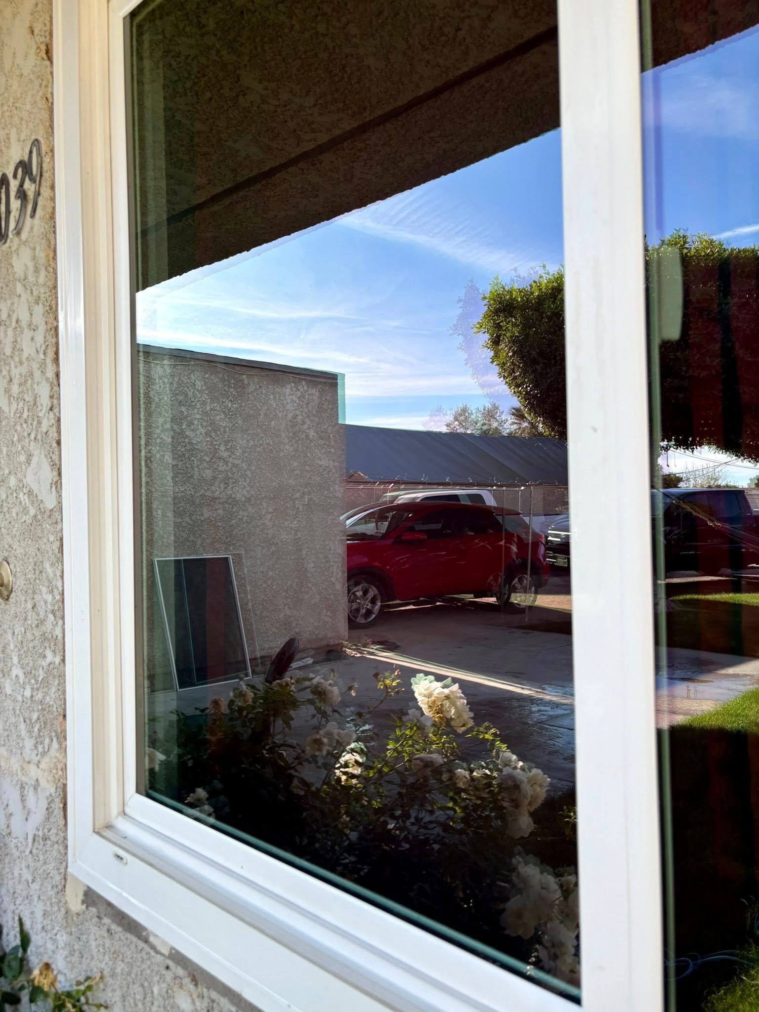 Window reflecting a red truck, blue sky, and house exterior in a sunny suburban setting