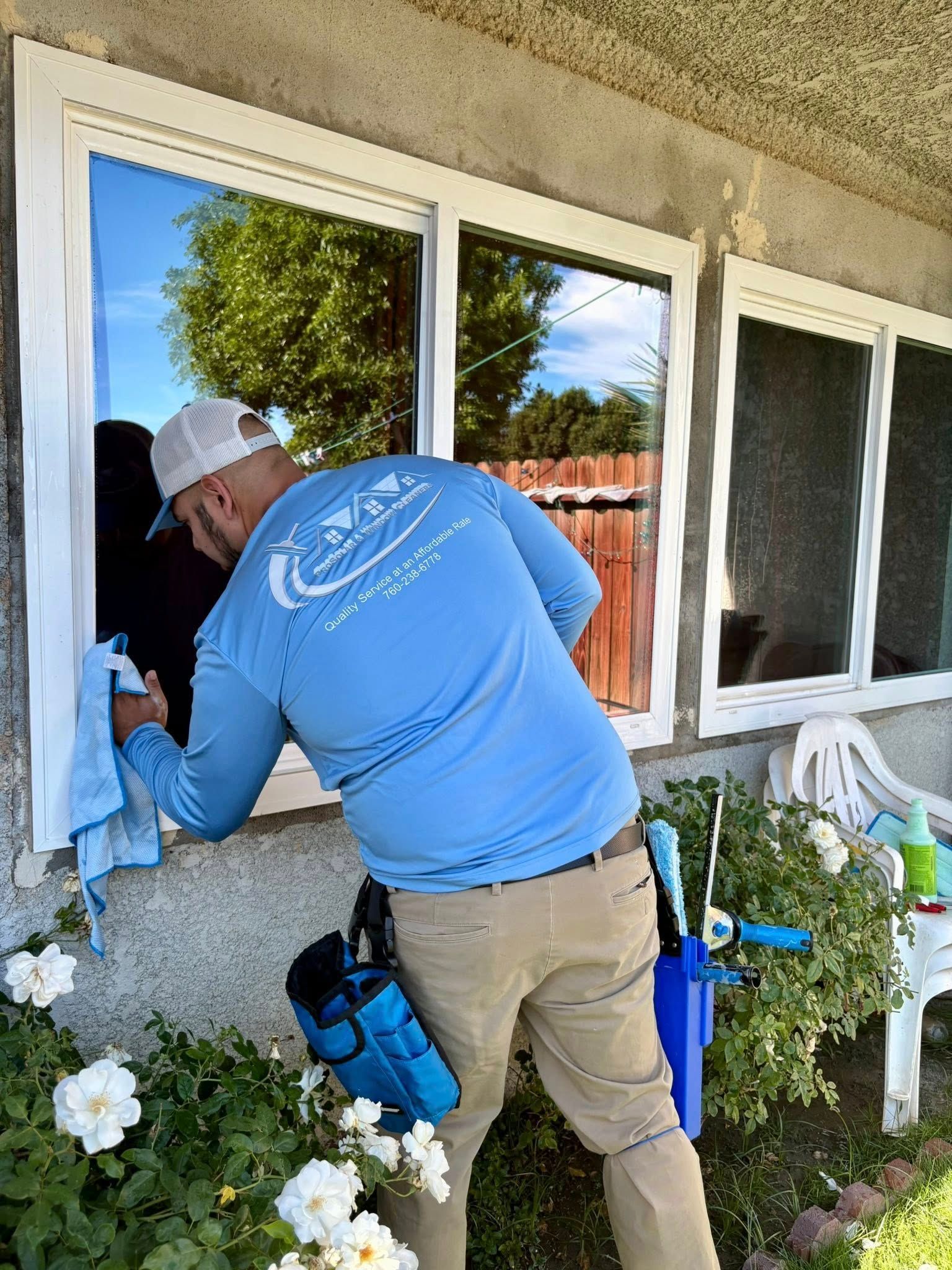 Worker in blue shirt inspecting a white window frame on a house exterior.