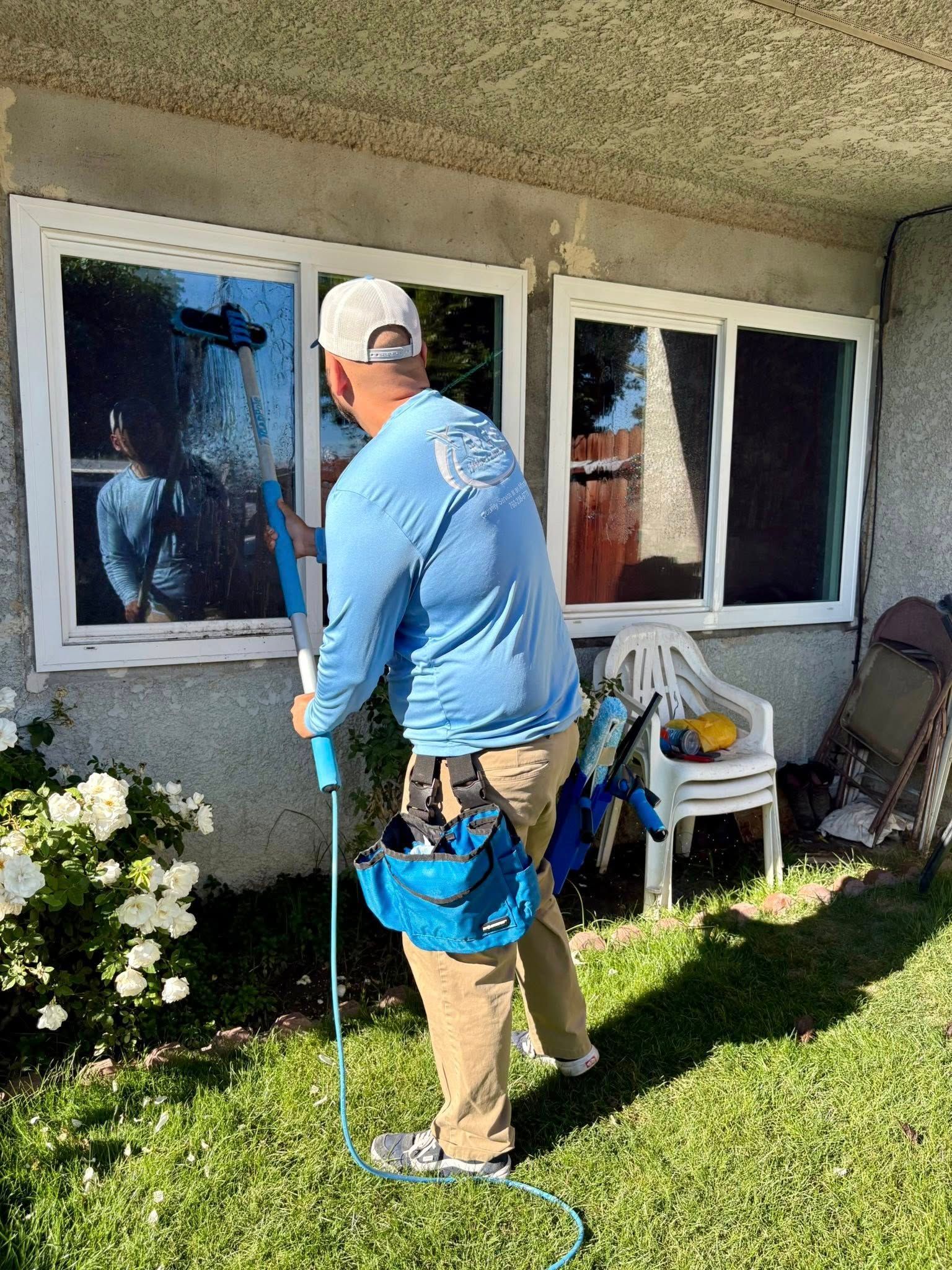 Person painting the exterior of a house beside white-framed windows, carrying a blue tool bag.