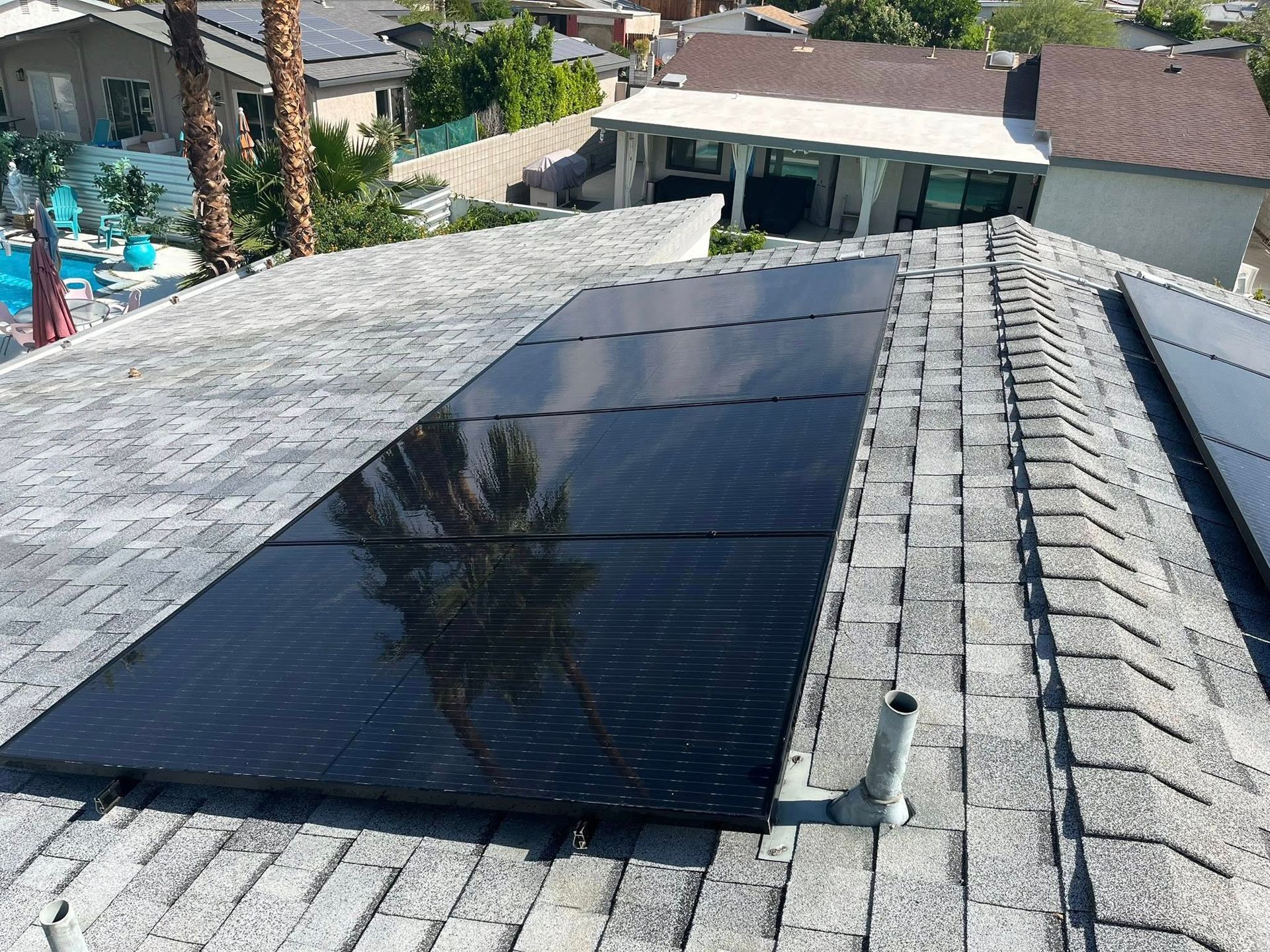 Solar panels installed on a sloped rooftop beside a shingled ridge and pool area