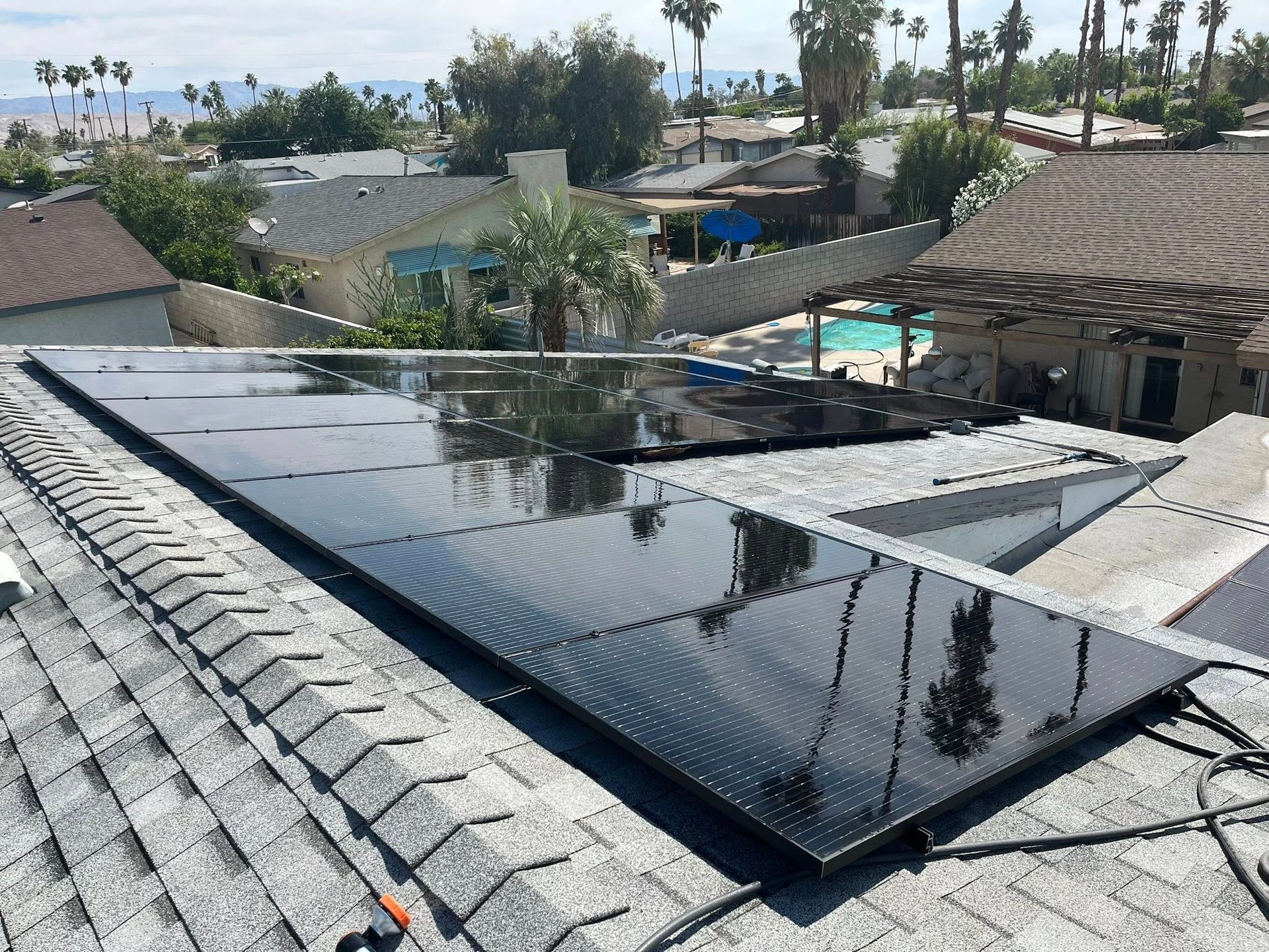 Solar panels on a rooftop overlooking a resort pool and palm trees with the ocean in the distance
