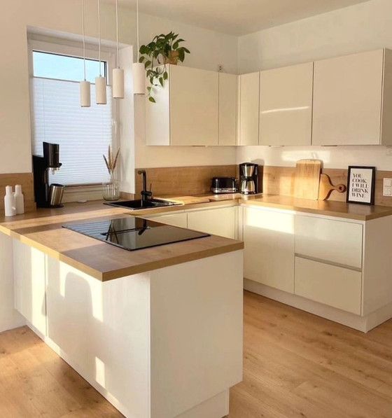A kitchen with white cabinets , wooden counter tops , a stove top oven , a sink , and a window.