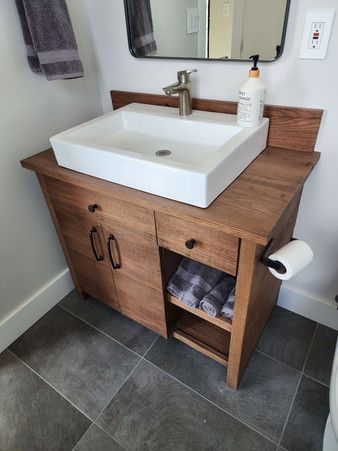 A bathroom with a wooden vanity , sink , mirror and toilet.