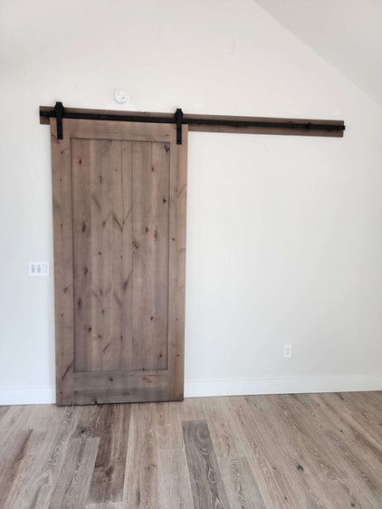 A sliding barn door is hanging on a white wall in an empty room.