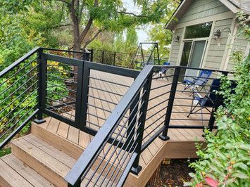 A wooden deck with a black railing and stairs leading up to it.