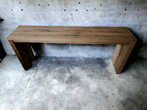 A wooden bench is sitting on a concrete floor in front of a concrete wall.