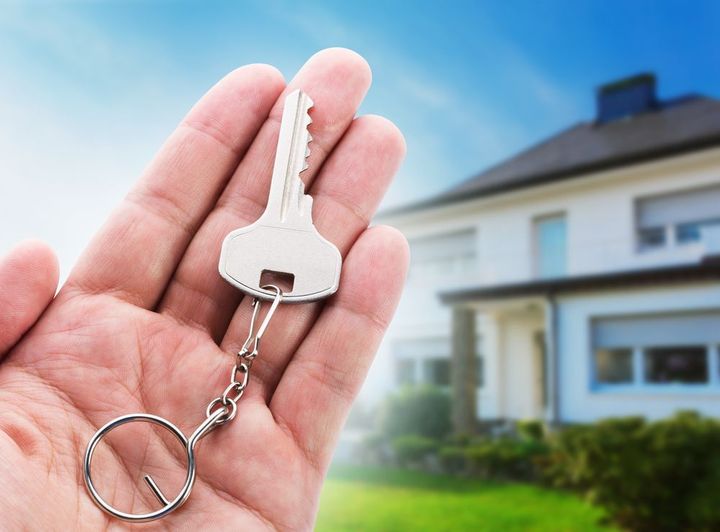A person is holding a key in front of a house.