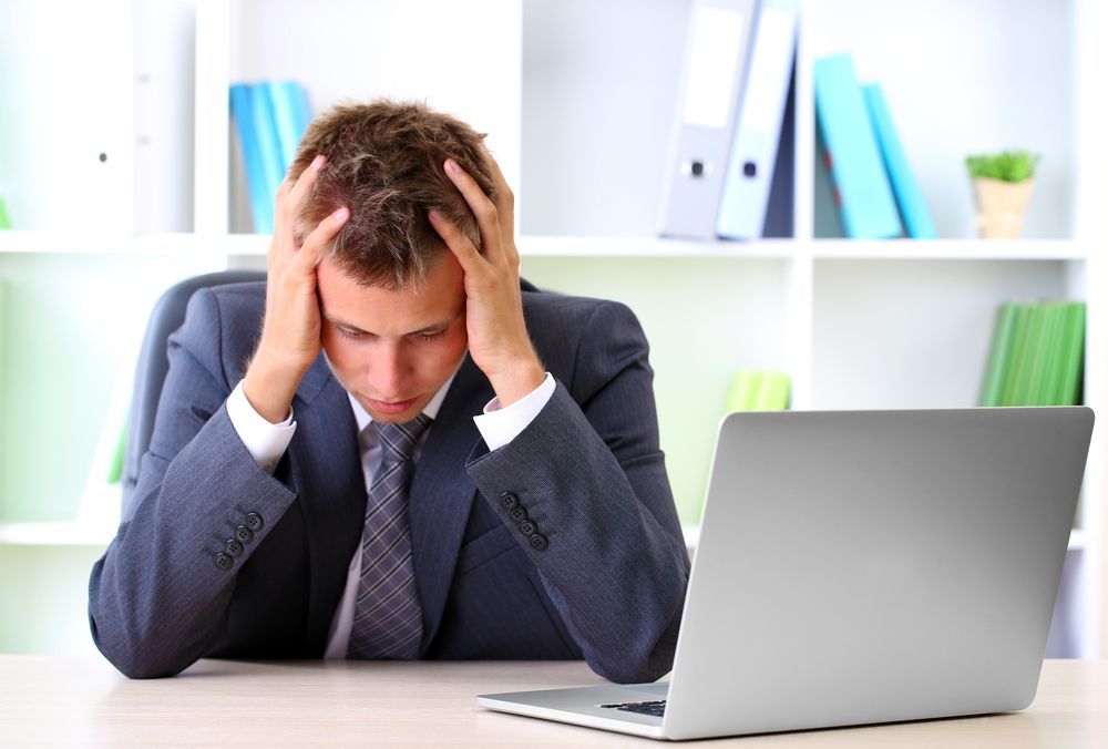 A man in a suit and tie is sitting at a desk in front of a laptop computer.