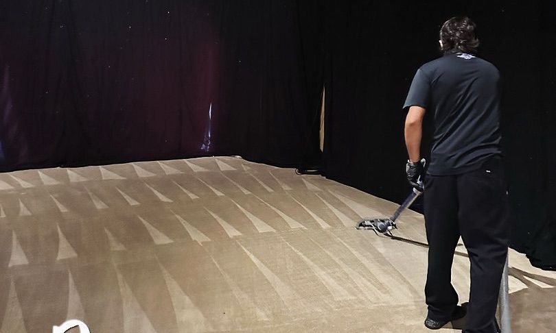 Person vacuuming a patterned carpet in a room with black walls.