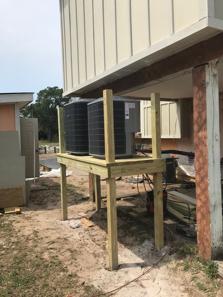 Two air conditioners are sitting on a wooden platform under a building.