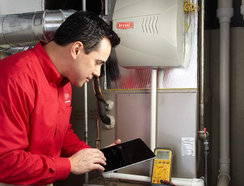 A man in a red shirt is looking at a tablet in front of a heater.