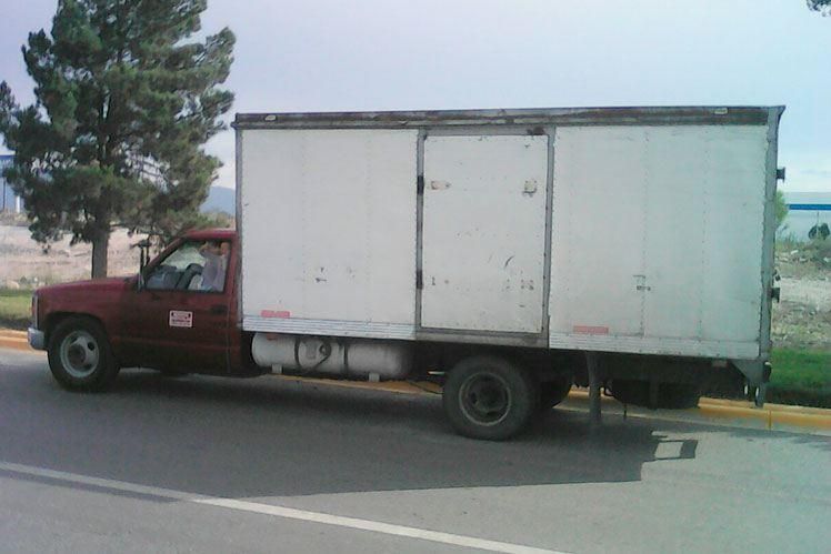 Un camión rojo con una caja blanca en la parte trasera está estacionado al costado de la carretera.