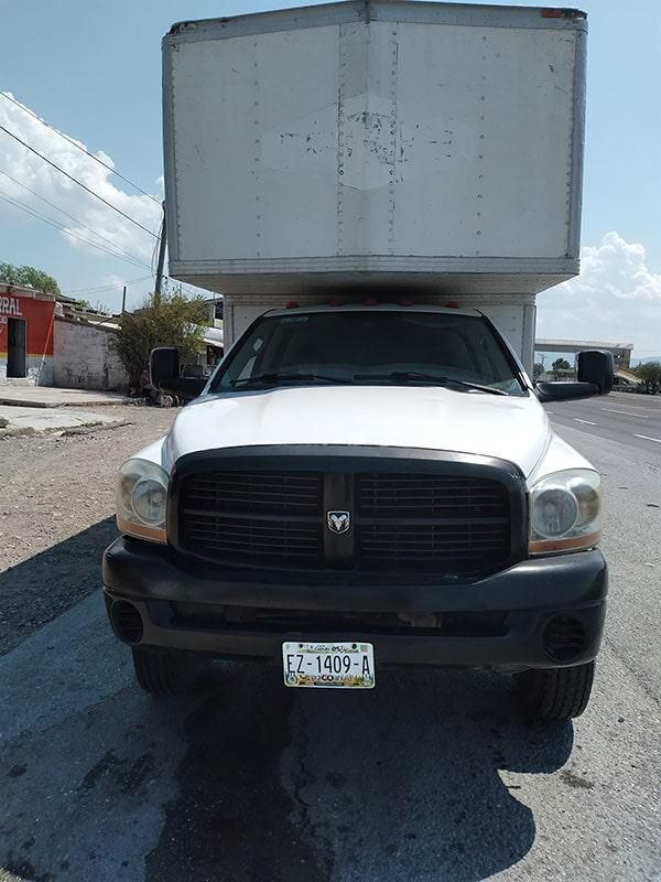 Un camión blanco con una caja encima está estacionado al costado de la carretera.