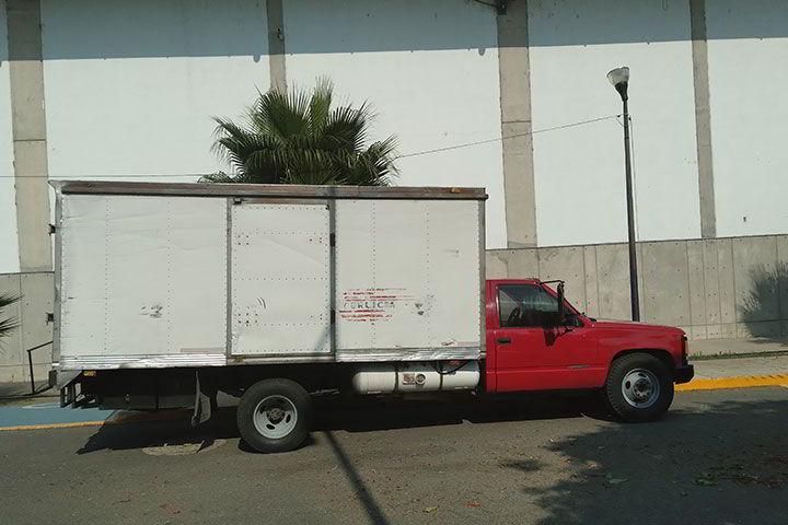 Un camión rojo con una caja blanca en la parte trasera está estacionado frente a un edificio.