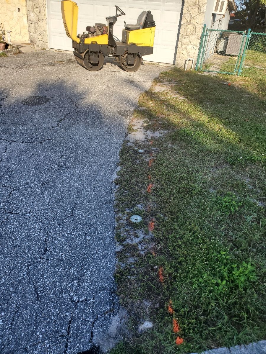 A yellow and black machine is parked on the side of the road next to a grassy area.