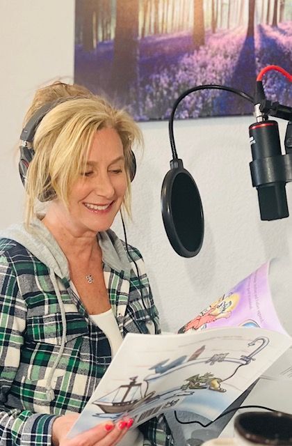 Woman recording a narration, wearing headphones and reading from a children's book, smiling.