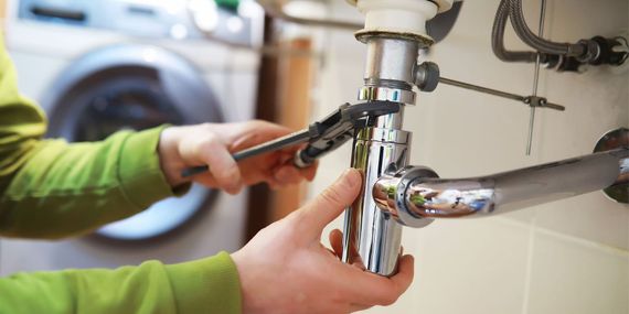 A person is fixing a sink pipe with a wrench.