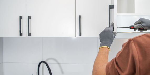 A man is fixing a kitchen cabinet with a screwdriver.