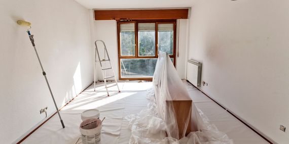 An empty room with a ladder and a bucket of paint.