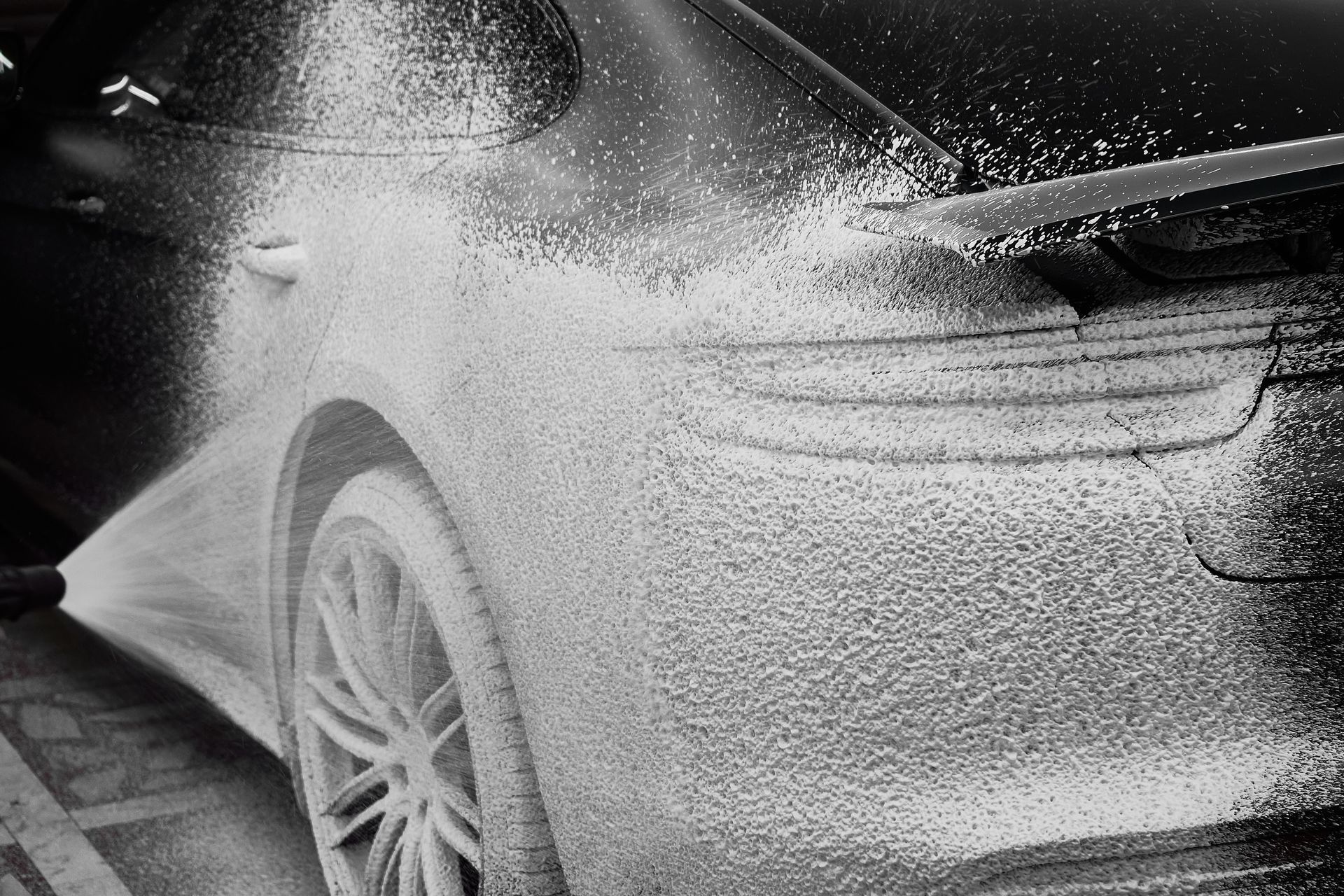 Car being sprayed with foamy soap at a carwash.