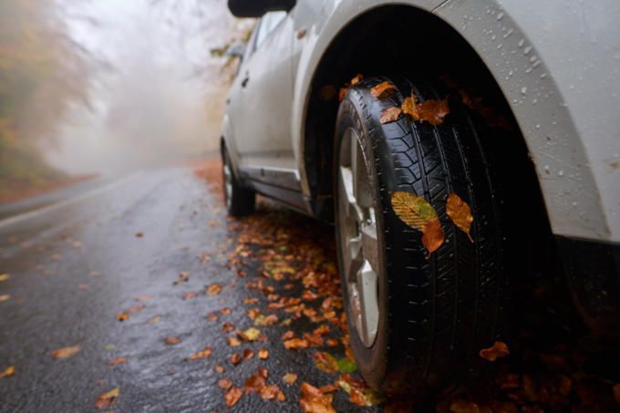 White car wheel on a rainy road, with fallen autumn leaves scattered along the wet pavement.