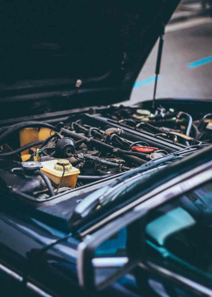 Car engine bay with hood open, showing exposed hoses and components in a dark-colored vehicle.