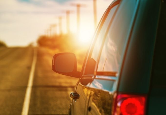 Car side mirror and taillight on a sunlit road at sunset