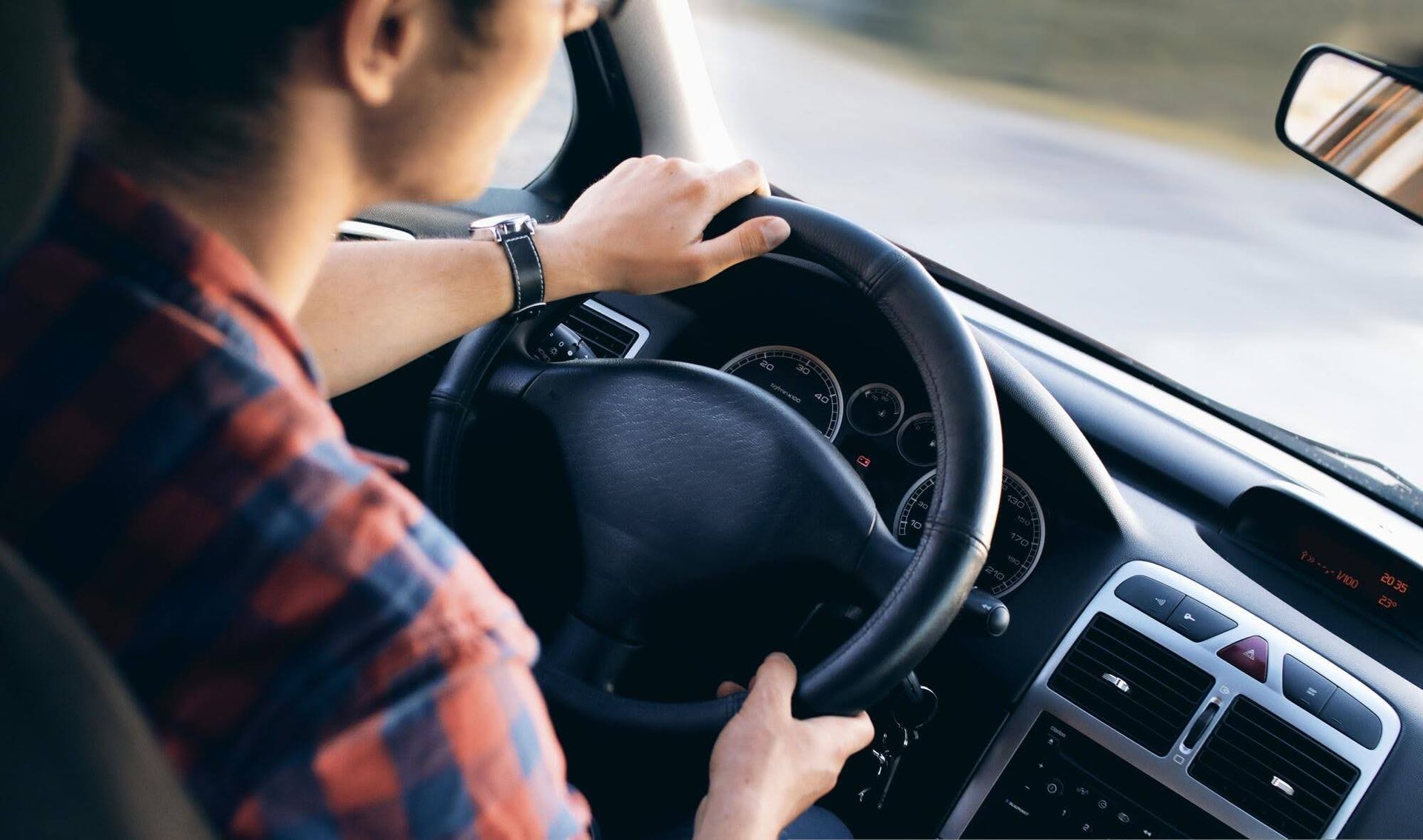 Driver holding steering wheel inside a car, with dashboard and windshield visible