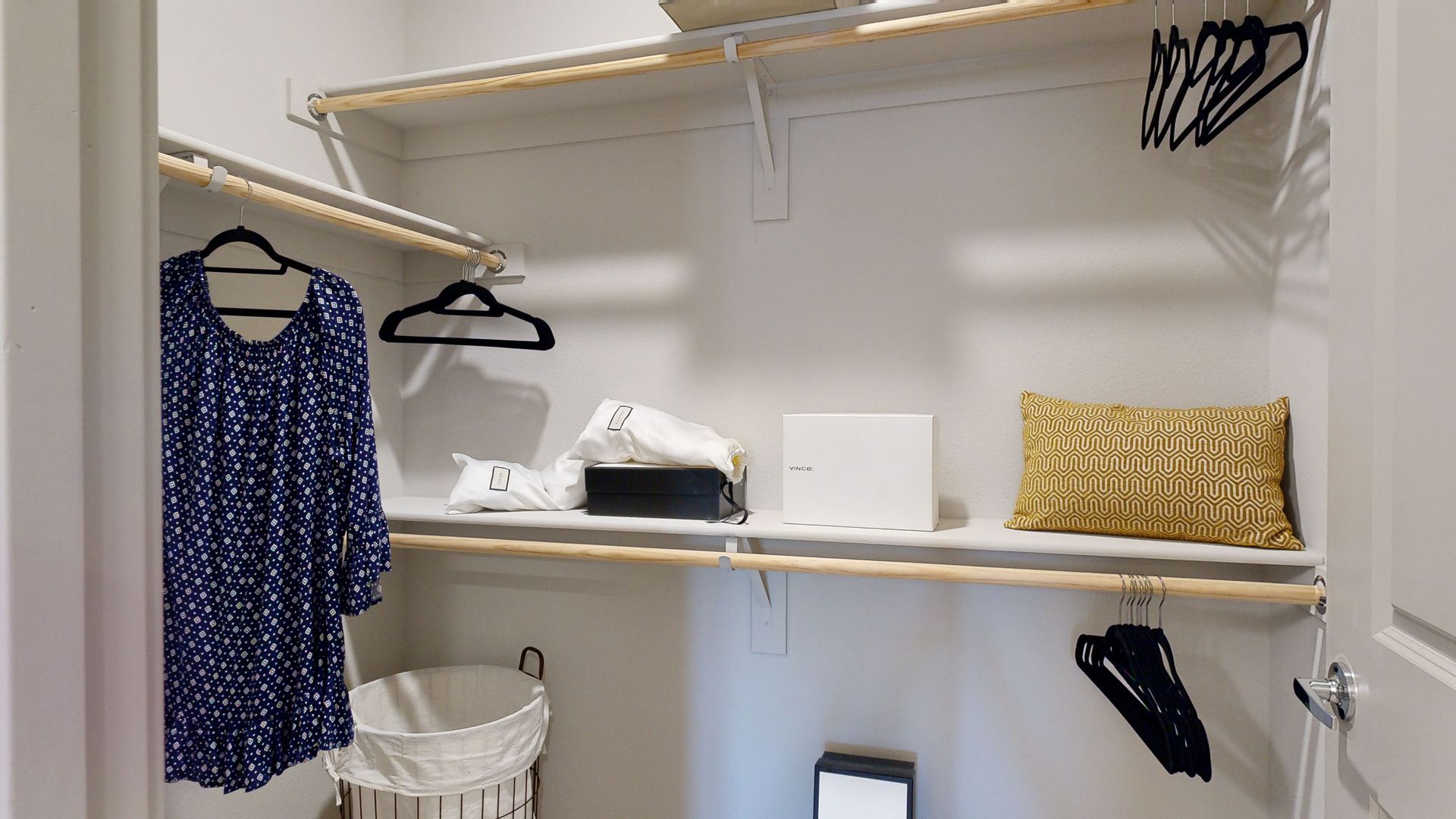 A walk in closet with clothes hanging on the shelves and a laundry basket.