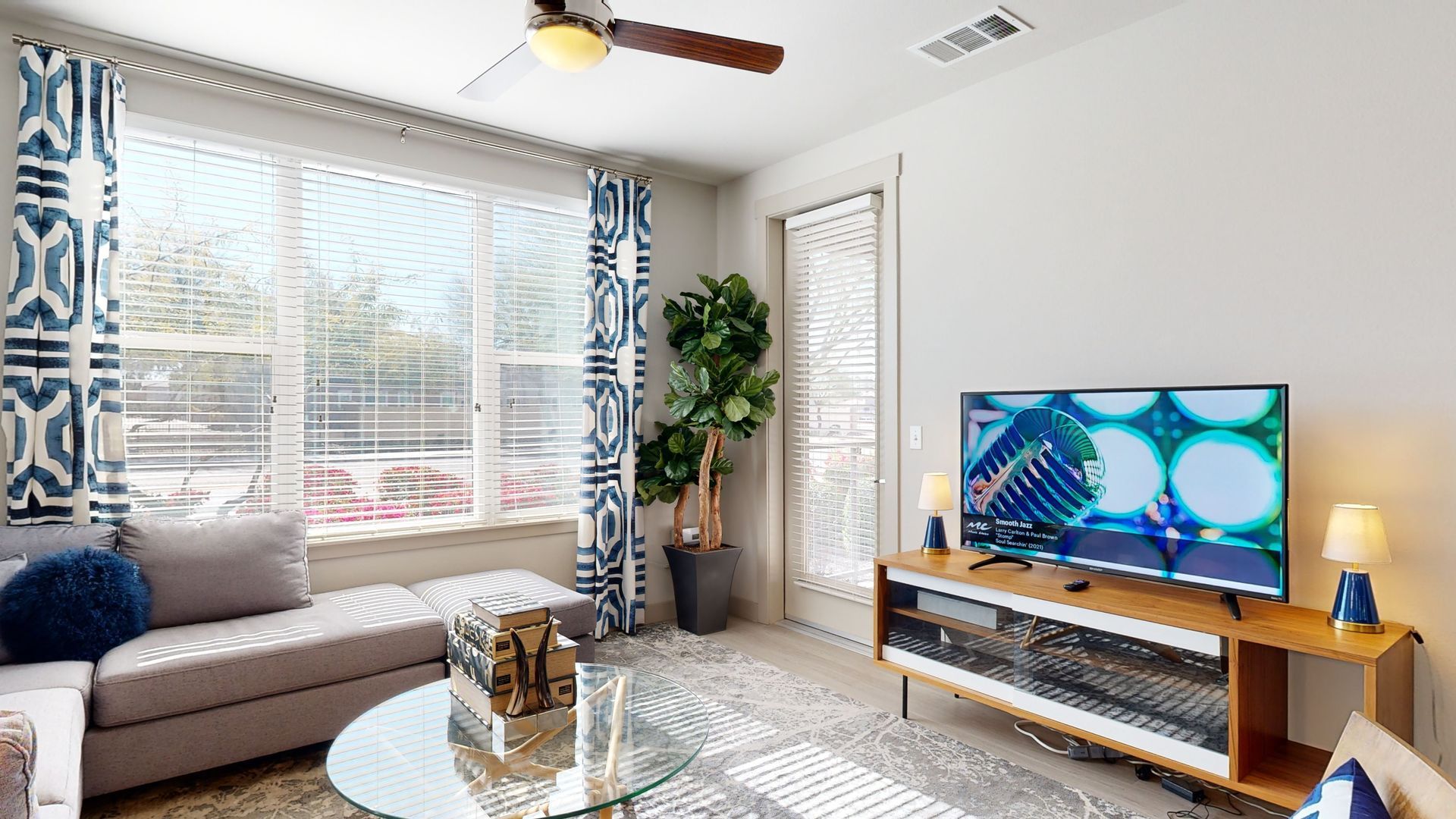 A living room with a couch , television , coffee table and ceiling fan.