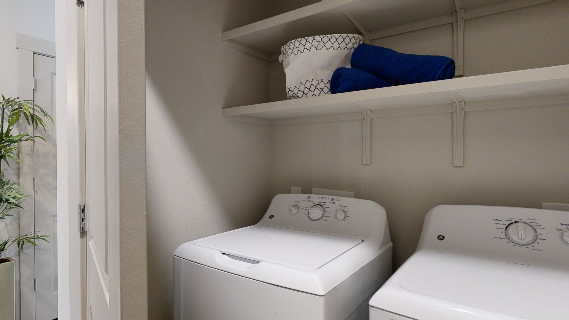 A laundry room with a washer and dryer and a shelf.