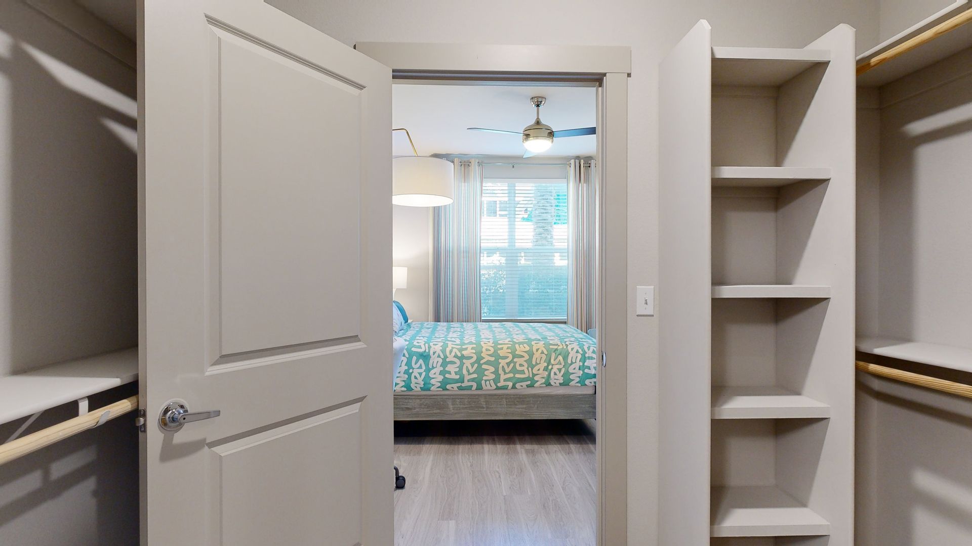 A walk in closet in a bedroom with a bed and a ceiling fan.