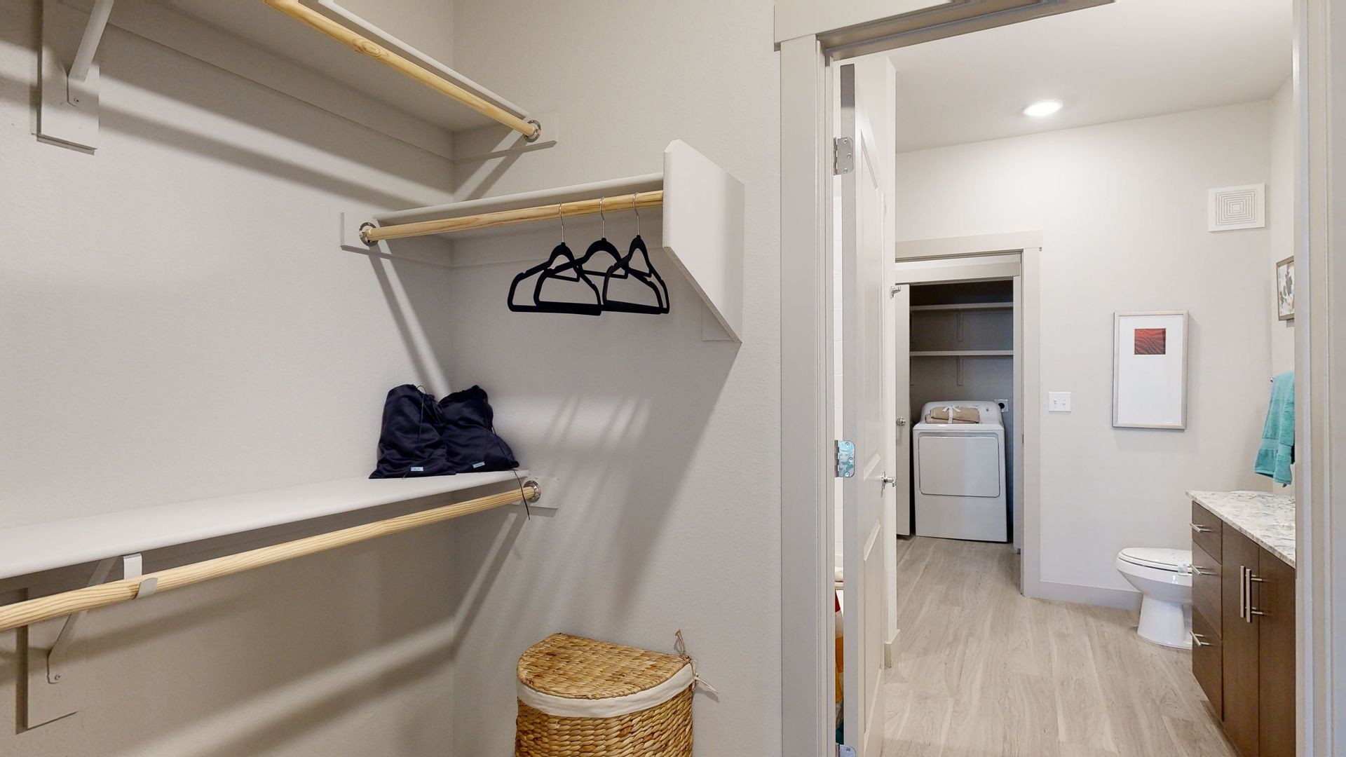 A walk in closet with clothes hanging on the shelves and a laundry basket.