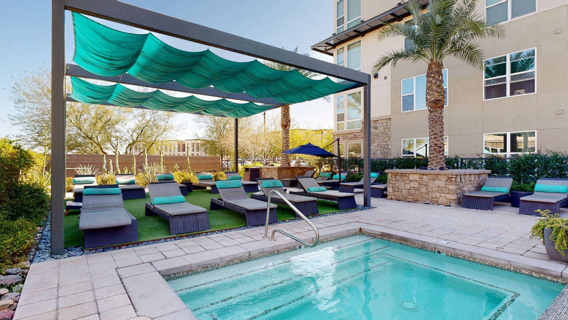 A large swimming pool surrounded by chairs and umbrellas in front of a building.