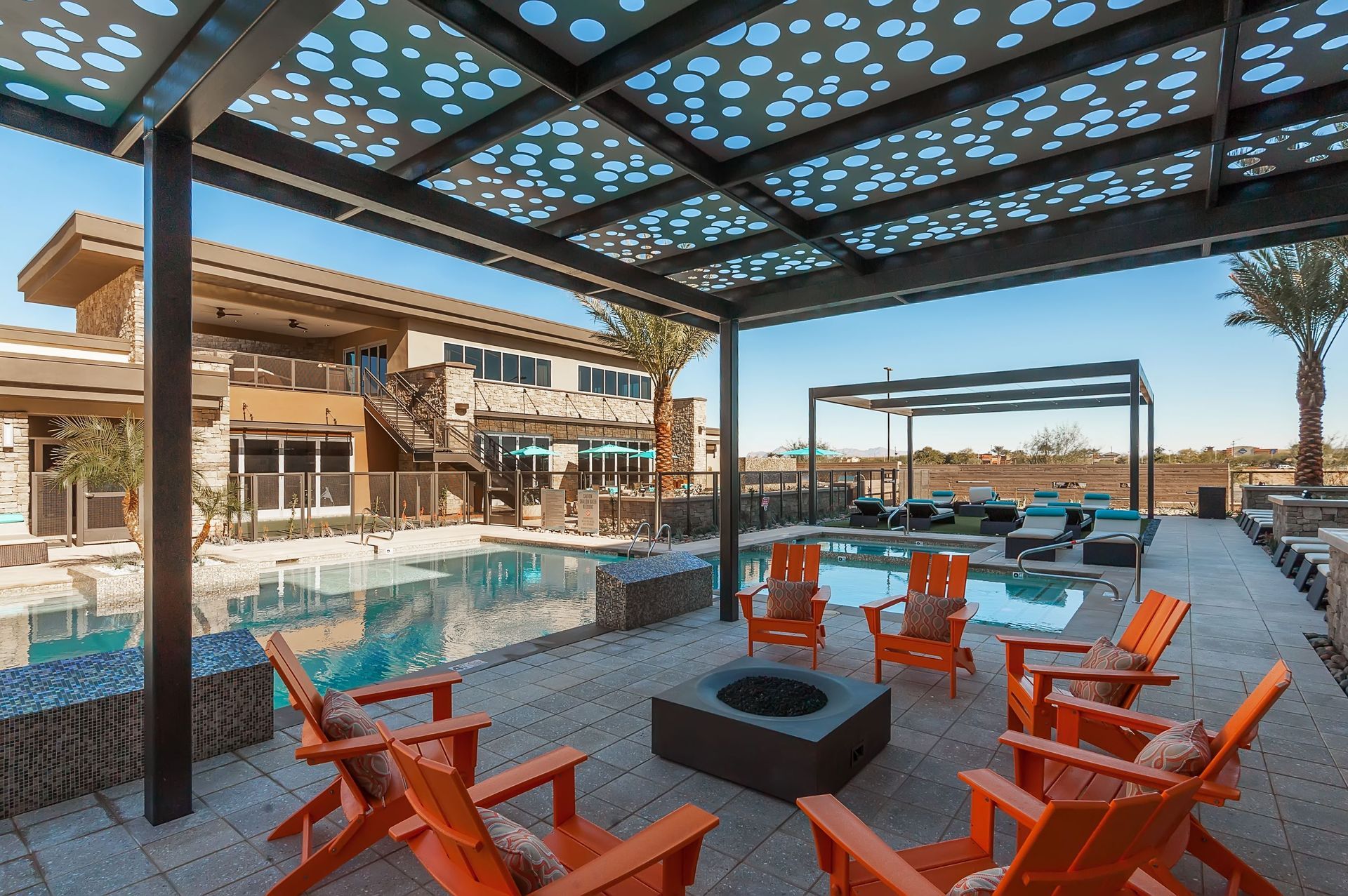 A patio area with chairs and a fire pit next to a swimming pool.