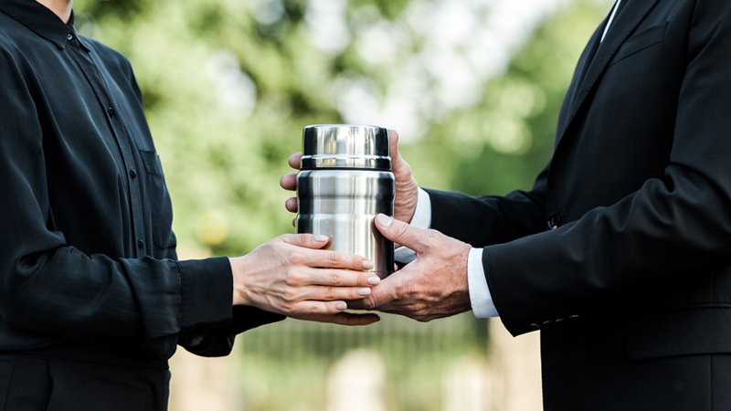Two people holding a cremation urn up close with focus on silver urn