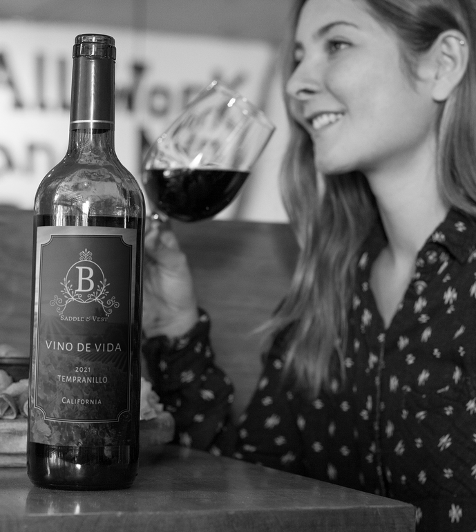 Bottle of red wine next to a woman smiling and holding a glass of wine. Black and white.