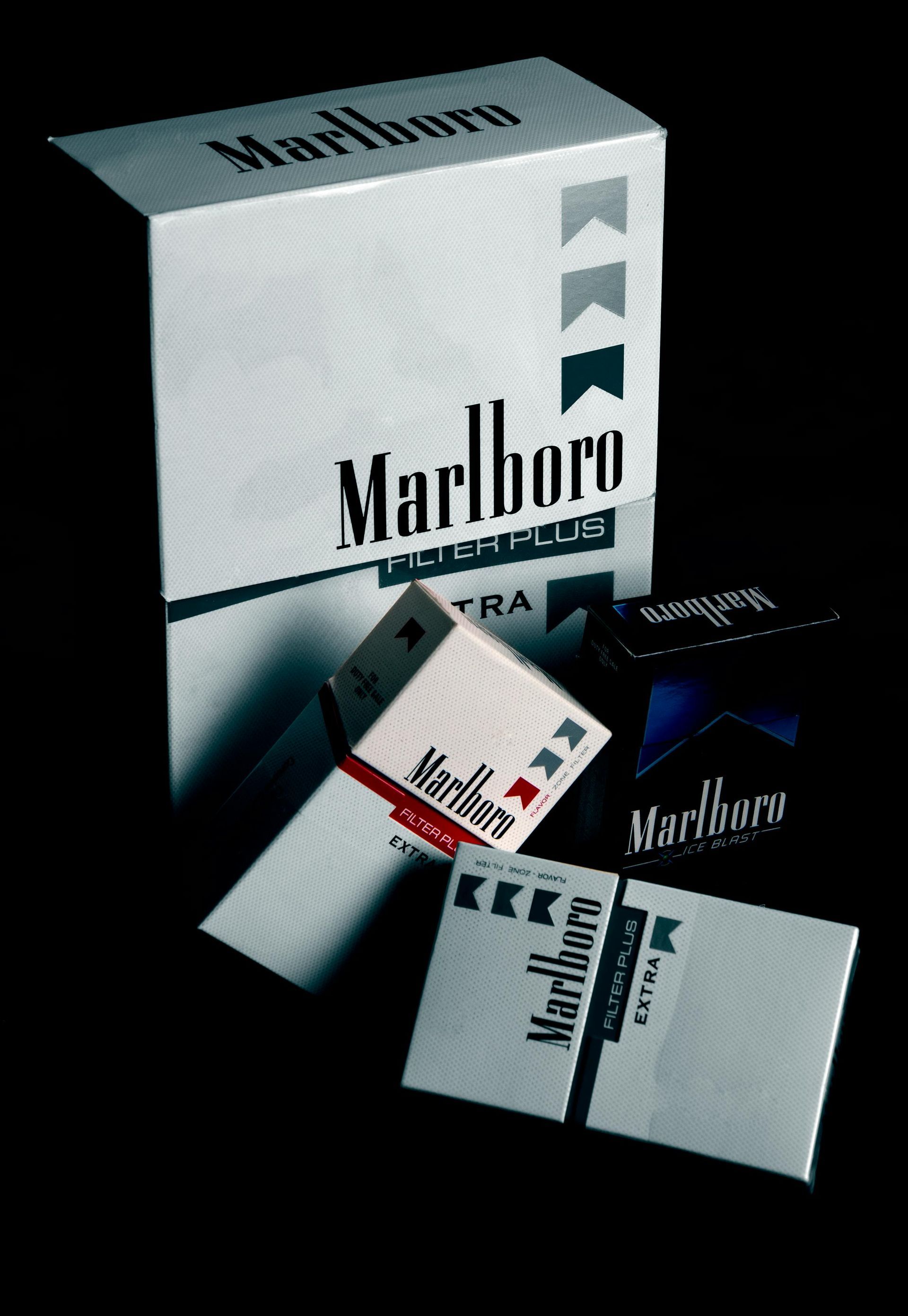Various packs of Marlboro cigarettes, mostly white with the brand logo and color-coded filters, in a dark setting.