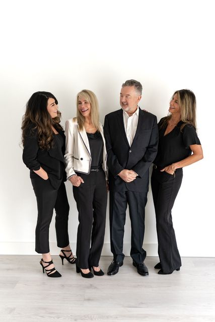 Four people stand against a white wall. Two women on either side of a man, all smiling. 