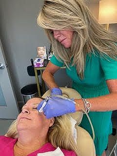 A woman in a green dress is giving a woman a facial treatment.