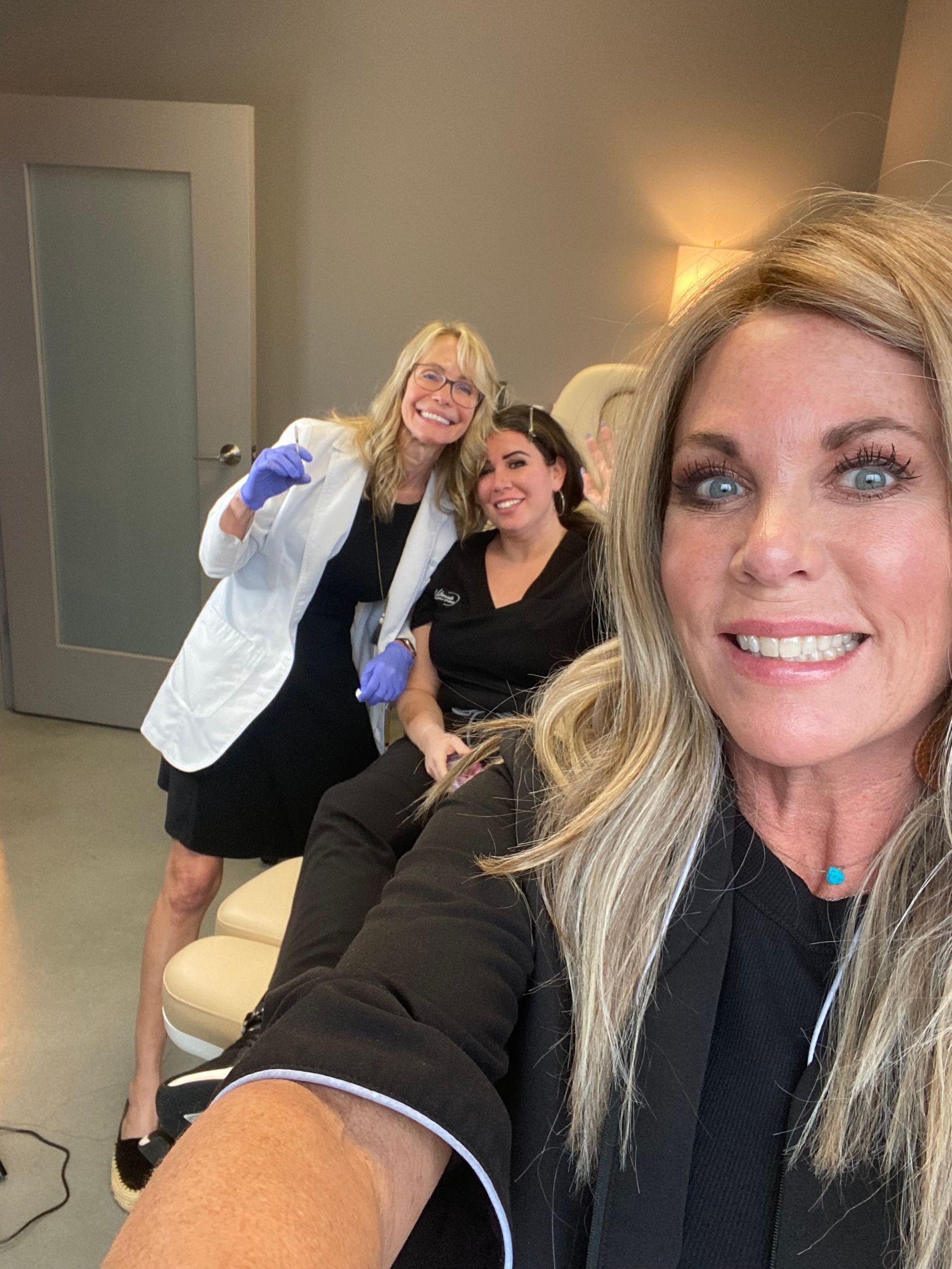 A woman is taking a selfie with two other women in a room.