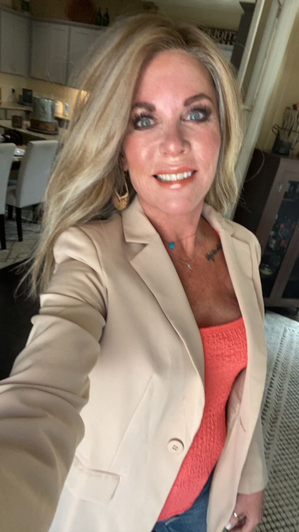 A woman is taking a selfie in a living room while wearing a tan blazer.