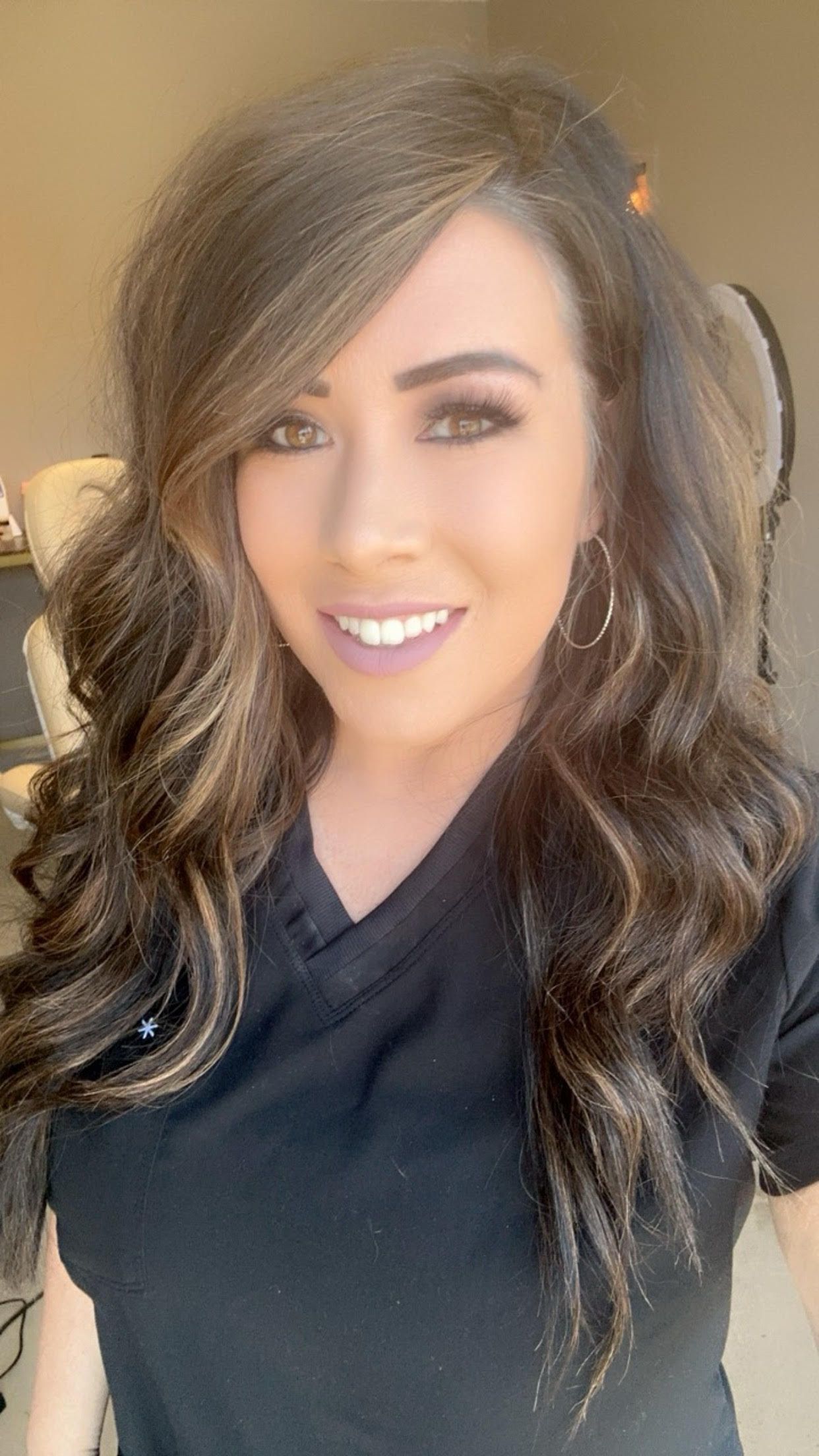 A woman wearing a black shirt and earrings is smiling for the camera.