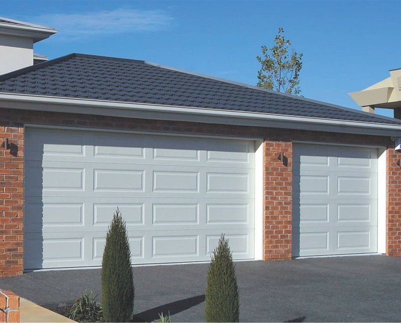 A house with three white garage doors and a brick wall
